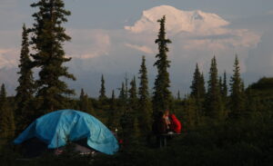 Campers sitting near a tent at Wonder Lake with Denali in the background