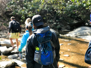 Day hikers with backpacks crossing a stream on a forest trail